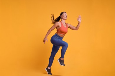 Woman in sportswear running on orange background