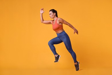 Photo of Woman in sportswear running on orange background