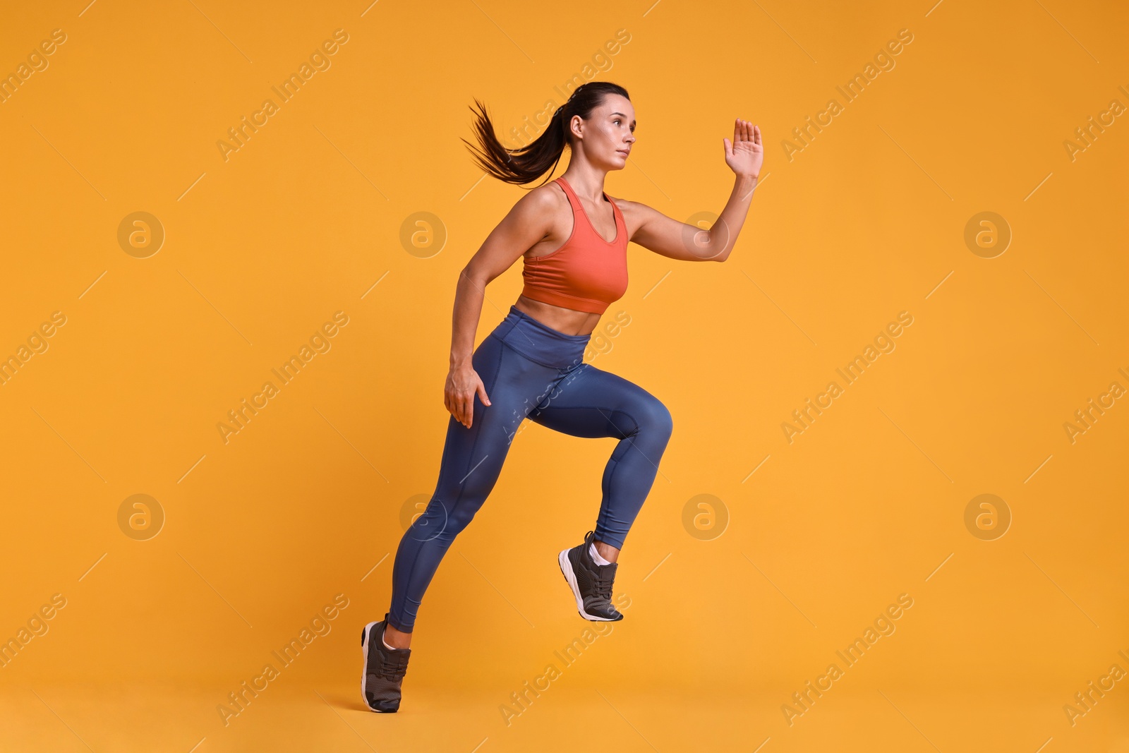 Photo of Woman in sportswear running on orange background