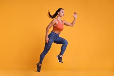 Woman in sportswear running on orange background