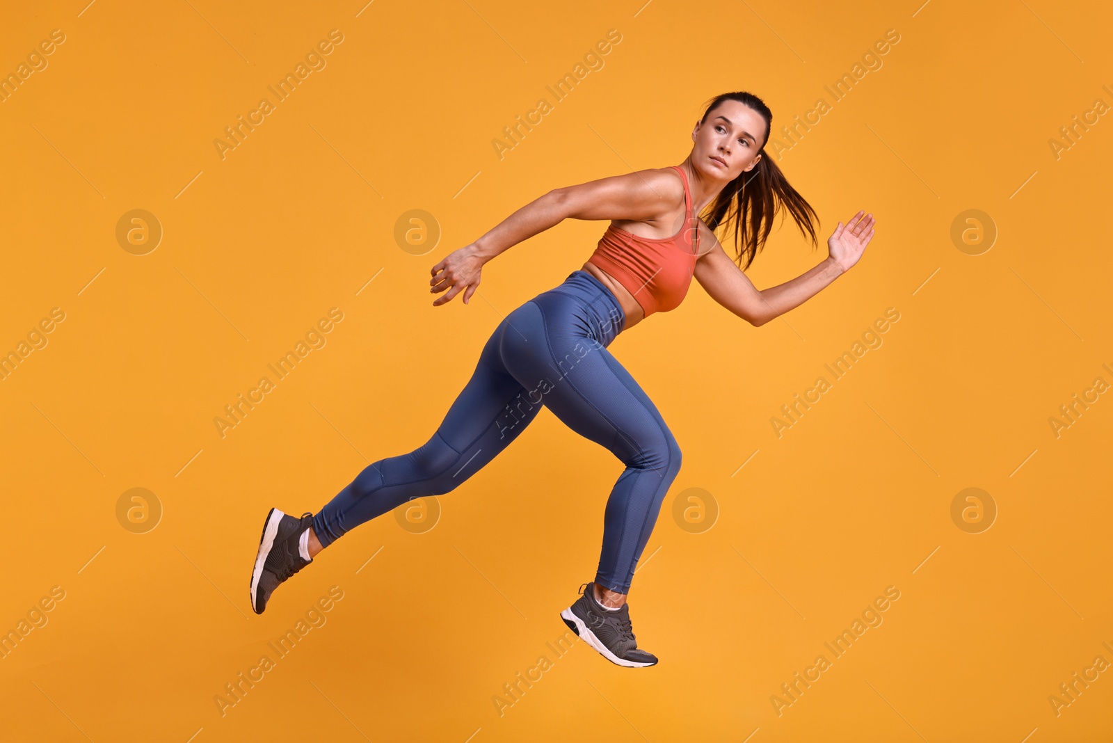 Photo of Woman in sportswear running on orange background