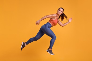 Woman in sportswear running on orange background