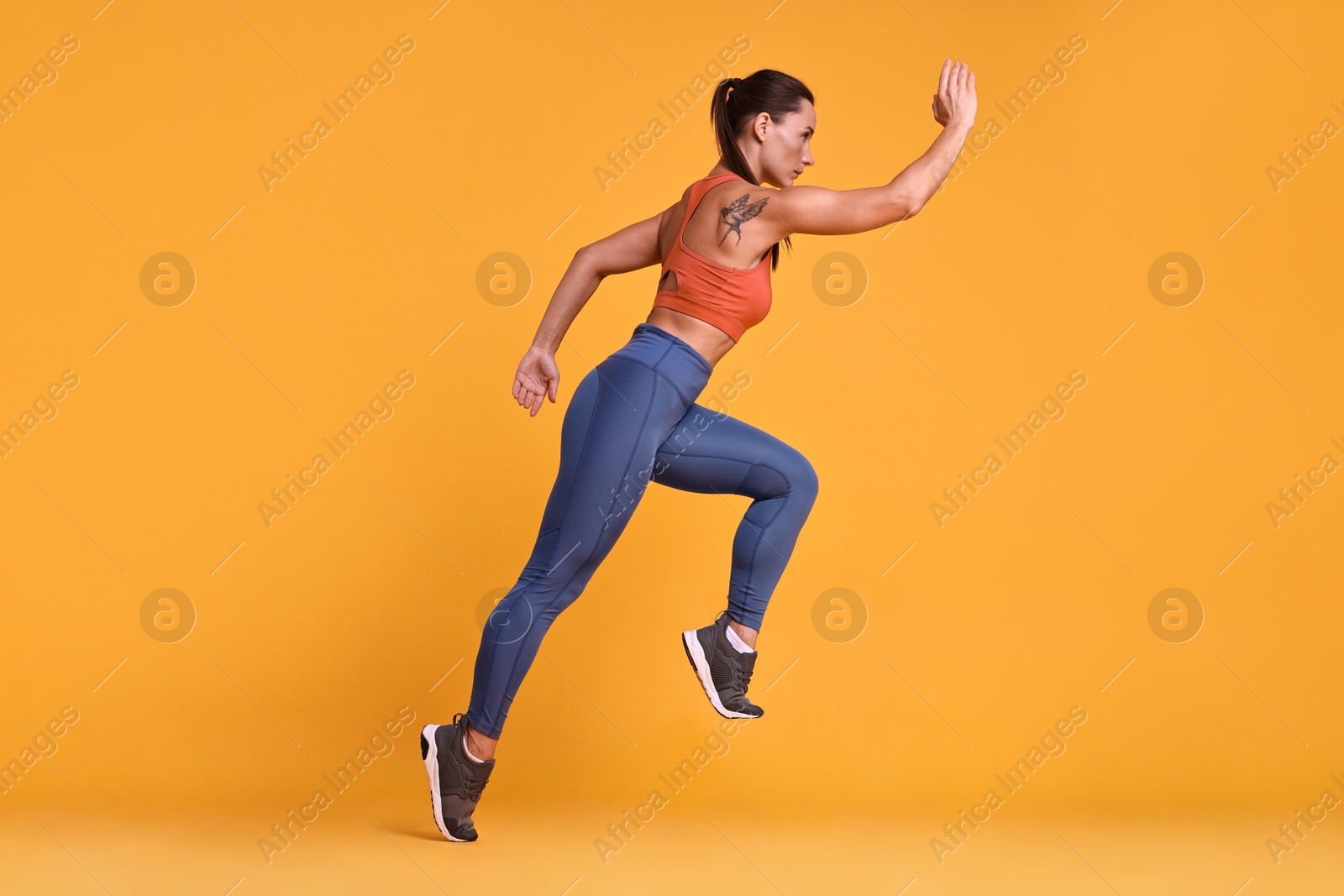 Photo of Woman in sportswear running on orange background