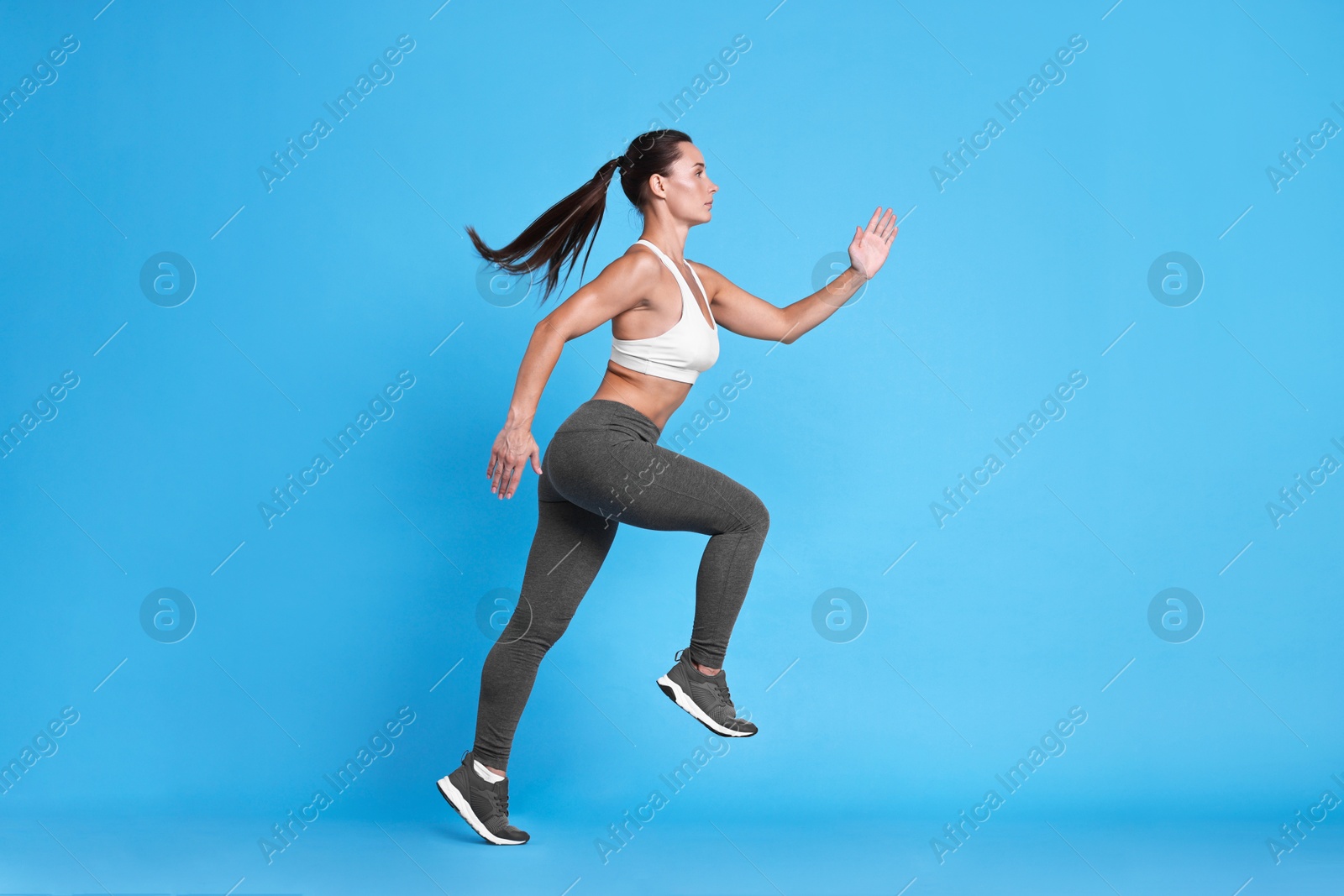 Photo of Woman in sportswear running on light blue background