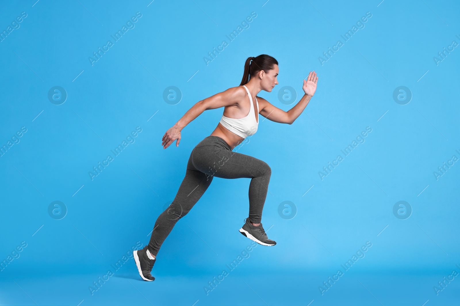 Photo of Woman in sportswear running on light blue background