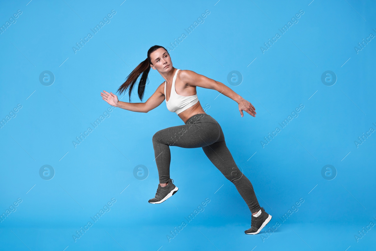 Photo of Woman in sportswear running on light blue background