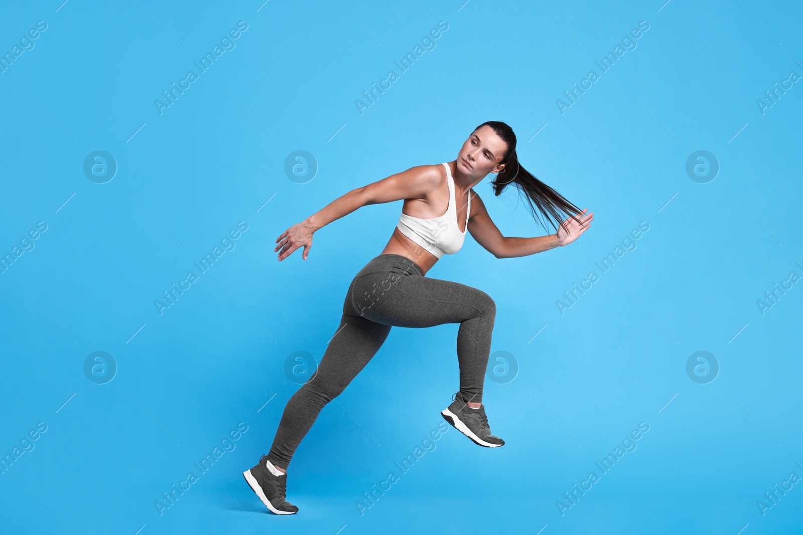 Photo of Woman in sportswear running on light blue background