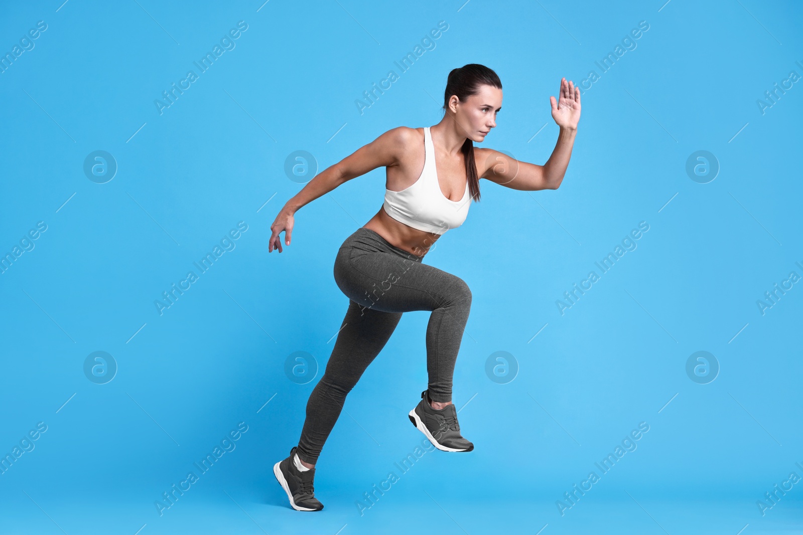 Photo of Woman in sportswear running on light blue background