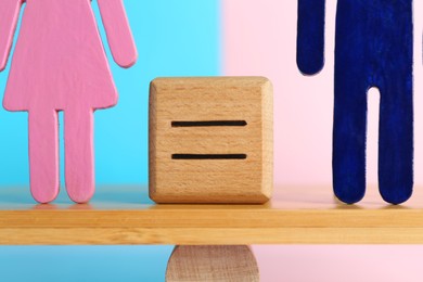 Gender equality concept. Cube with equals sign between male and female figures on scales against color background, closeup