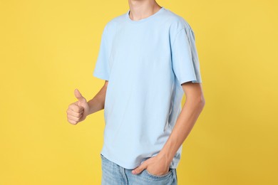 Photo of Teenage boy wearing light blue t-shirt and showing thumbs up on yellow background, closeup