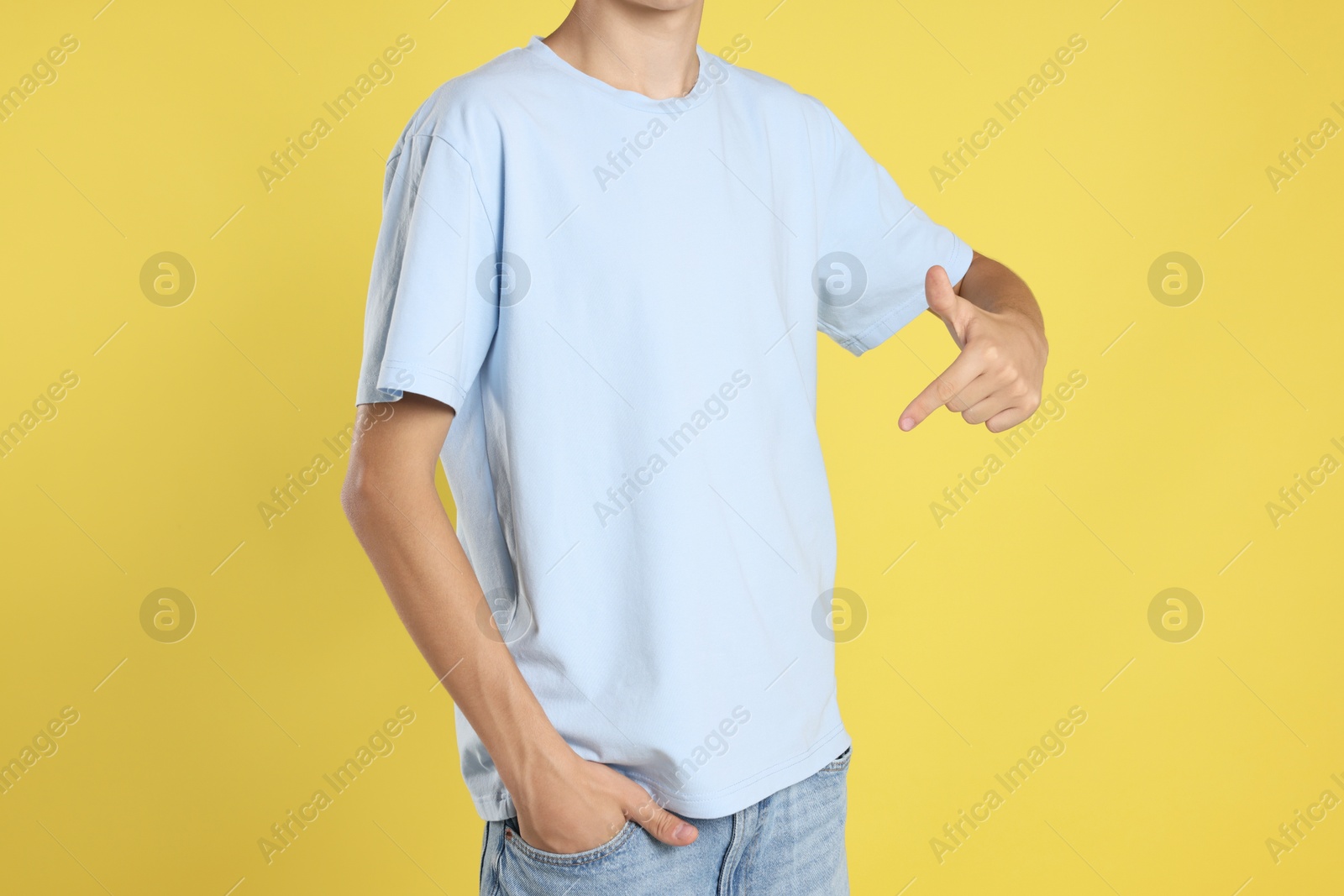 Photo of Teenage boy wearing light blue t-shirt on yellow background, closeup