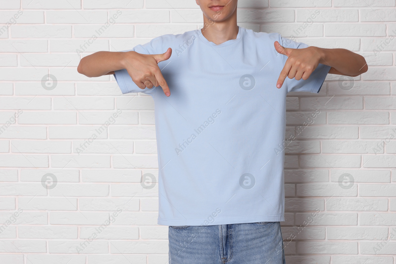 Photo of Teenage boy wearing light blue t-shirt near white brick wall, closeup