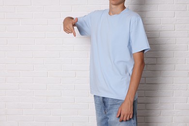 Photo of Teenage boy wearing light blue t-shirt near white brick wall, closeup. Space for text