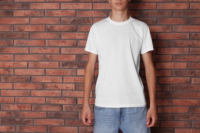 Teenage boy wearing white t-shirt near brick wall, closeup. Space for text