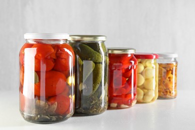 Photo of Tasty pickled vegetables and mushrooms in jars on white background, closeup