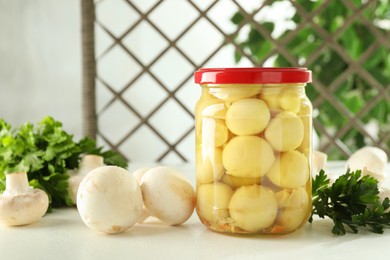 Photo of Tasty pickled mushrooms in jar and parsley on white table indoors