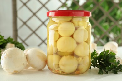 Photo of Tasty pickled mushrooms in jar and parsley on white table indoors, closeup