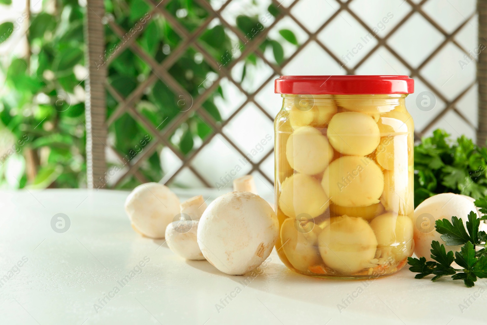 Photo of Tasty pickled mushrooms in jar and parsley on white table indoors, space for text