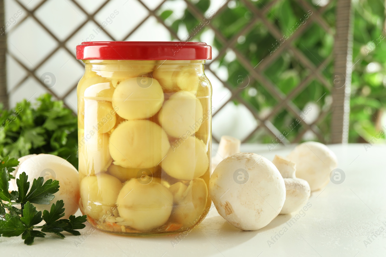 Photo of Tasty pickled mushrooms in jar and parsley on white table indoors. Space for text