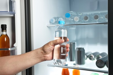 Photo of Woman taking bottle of water from refrigerator, closeup