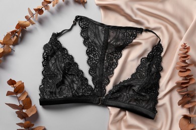 Photo of Beautiful lace bra and eucalyptus leaves on grey background, top view