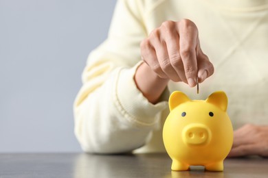 Photo of Woman putting coin into piggy bank at wooden table, closeup