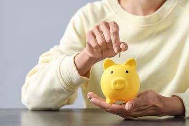 Woman putting coin into piggy bank at wooden table, closeup