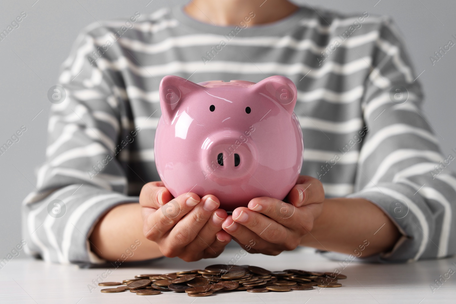 Photo of Woman holding piggy bank over white wooden table with coins, closeup