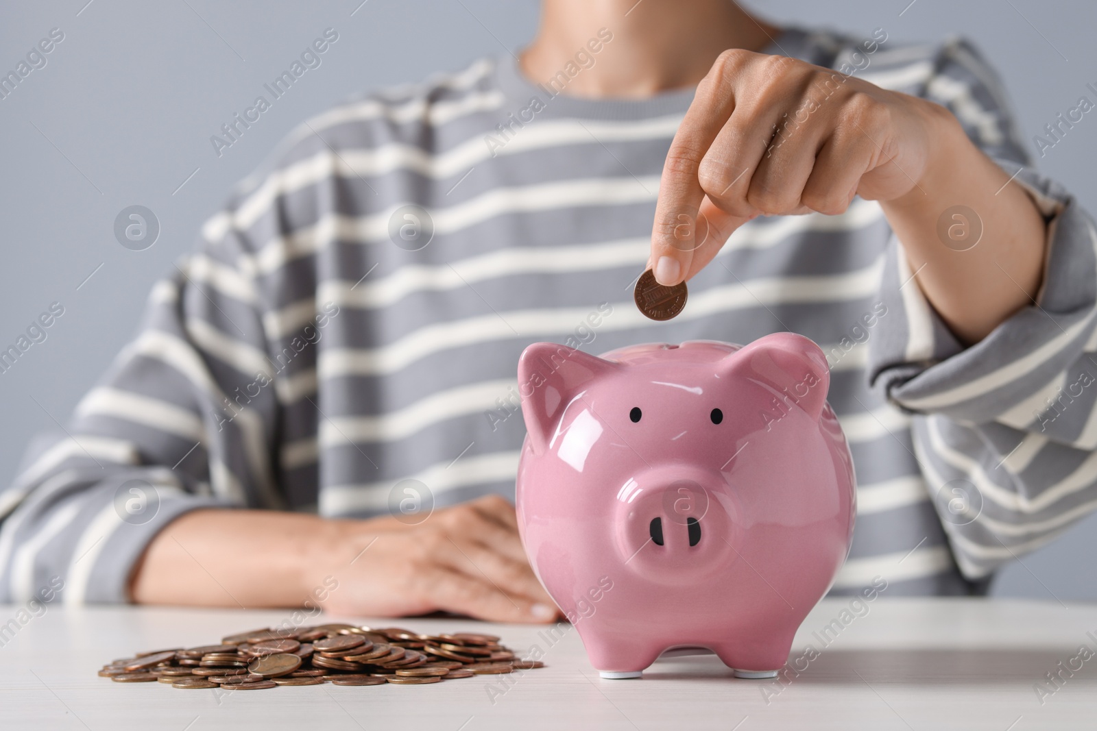 Photo of Woman putting coin into piggy bank at white wooden table, closeup