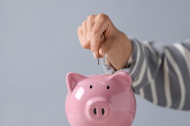 Photo of Woman putting coin into piggy bank against grey background, closeup