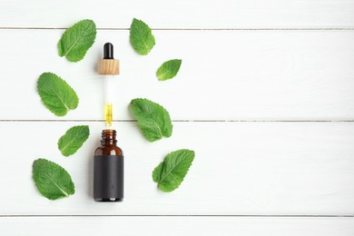 Photo of Dripping tincture from pipette into bottle and mint on white wooden table, flat lay. Space for text