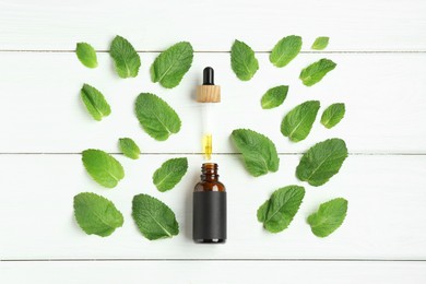 Photo of Dripping tincture from pipette into bottle and mint on white wooden table, flat lay