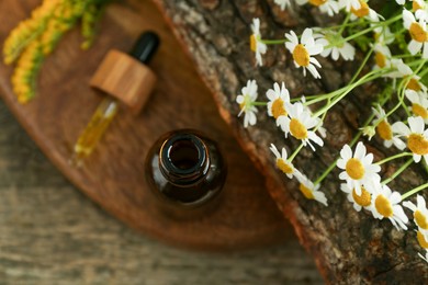 Photo of Tincture in bottle, pipette, goldenrods and chamomile flowers on wooden table, above view