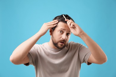 Man brushing his hair on light blue background. Alopecia problem