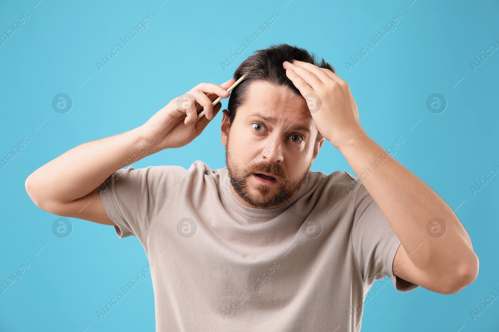 Photo of Man brushing his hair on light blue background. Alopecia problem