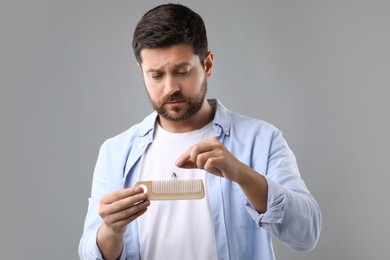 Sad man taking his lost hair from comb on gray background. Alopecia problem