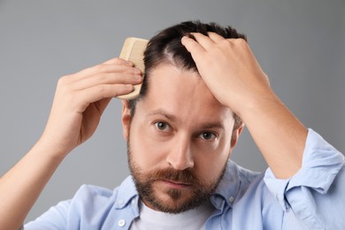 Man brushing his hair on gray background. Alopecia problem