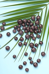 Photo of Ripe acai berries and palm leaves on light blue background, flat lay