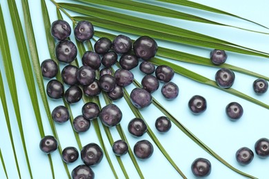 Ripe acai berries and palm leaves on light blue background, flat lay