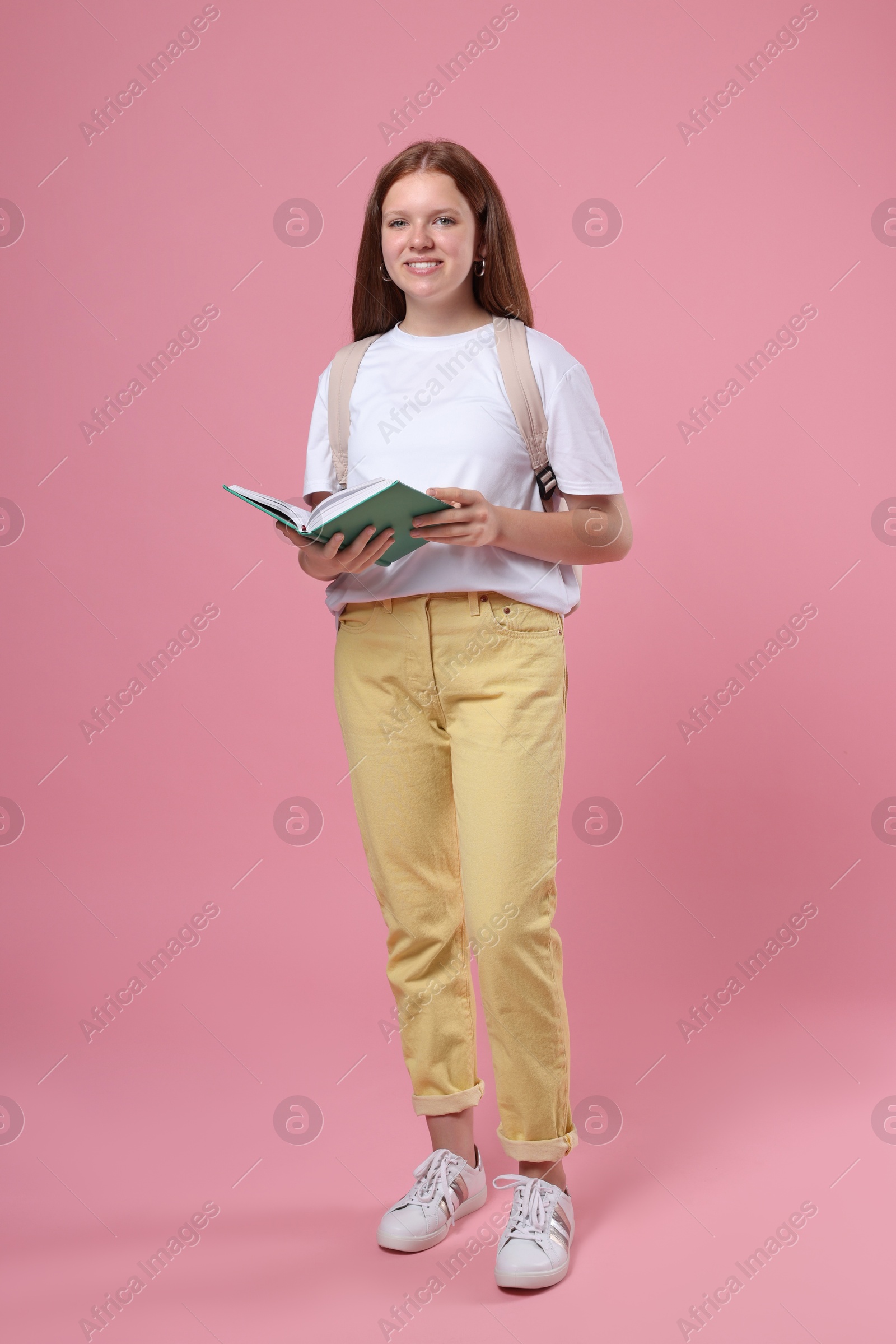 Photo of Teenage girl with backpack and open book on pink background