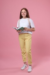 Photo of Teenage girl with backpack and open book on pink background