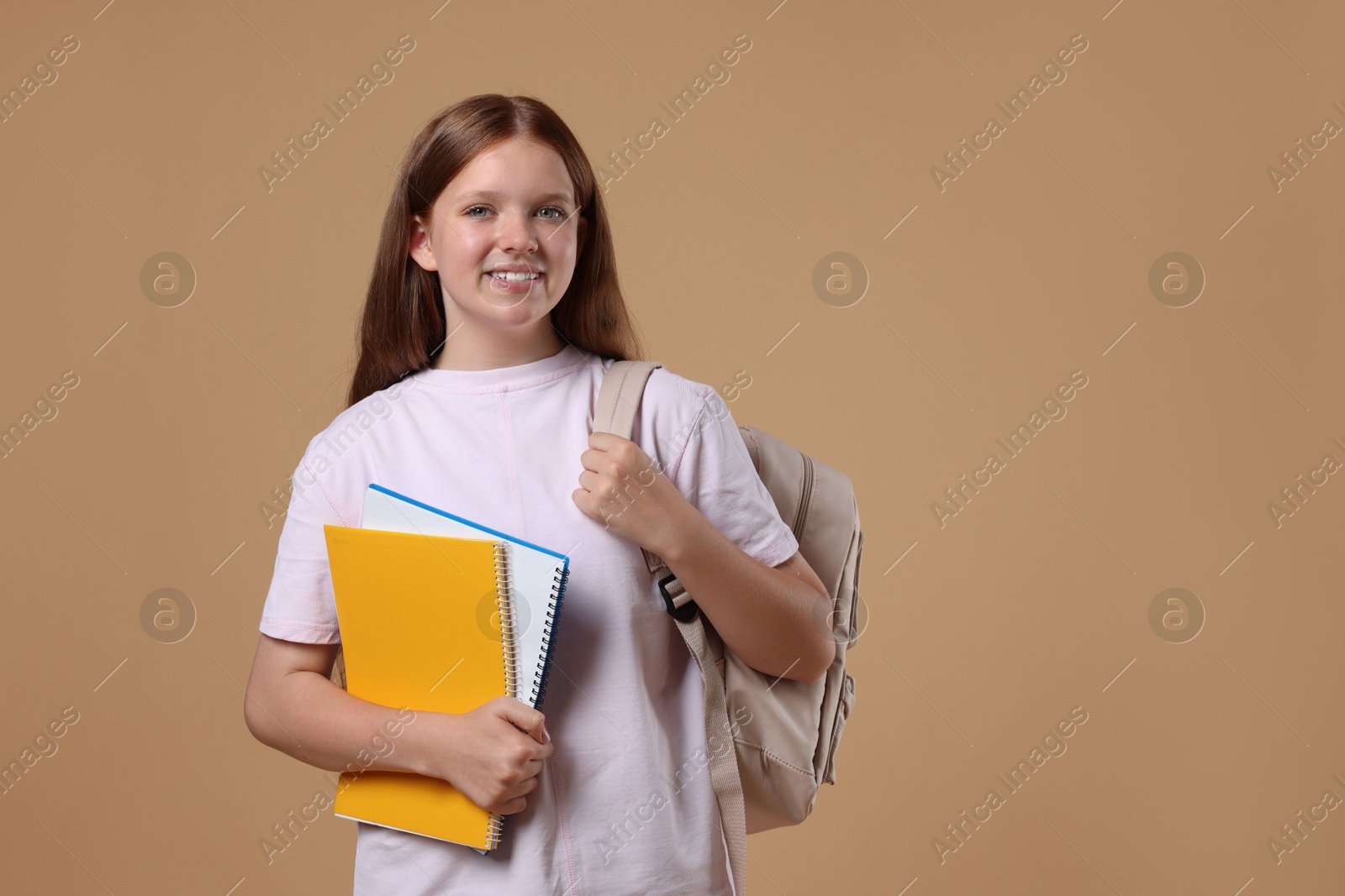 Photo of Teenage girl with backpack and books on beige background, space for text