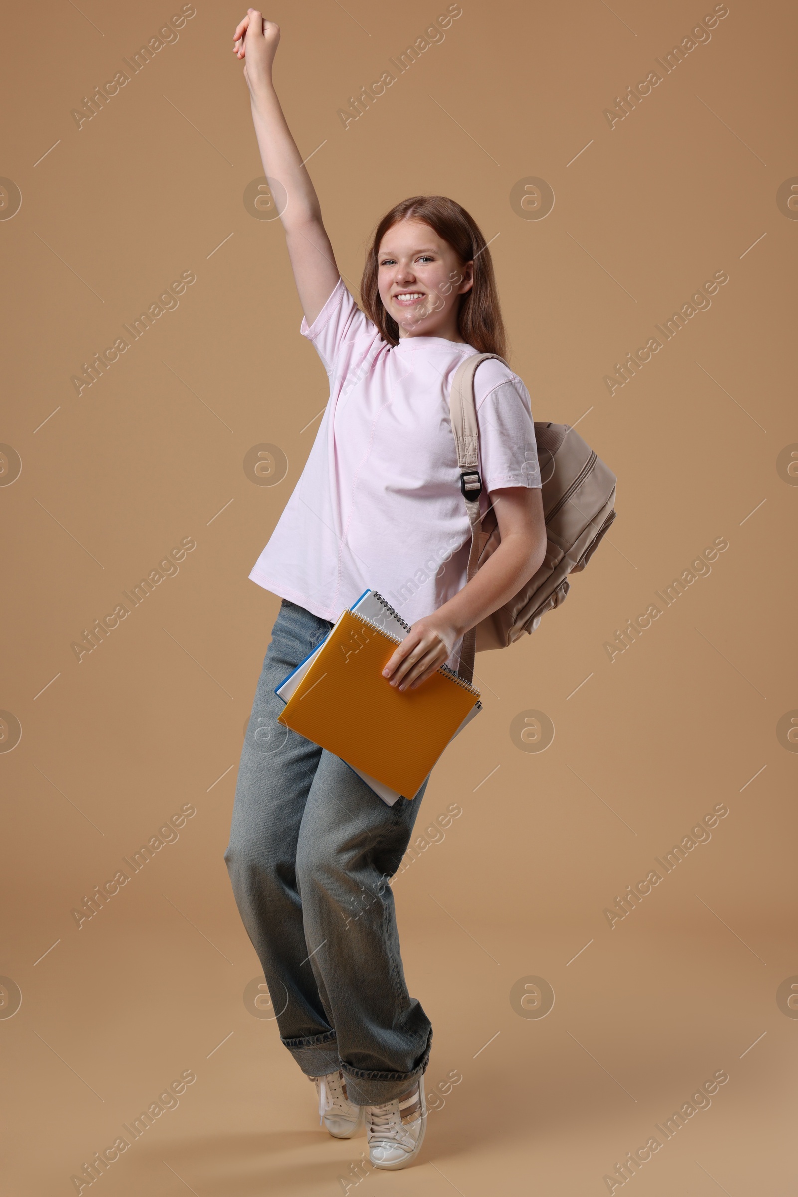 Photo of Teenage girl with backpack and books on beige background