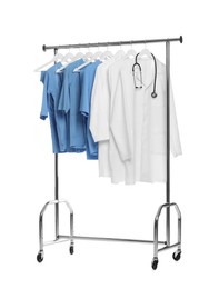 Photo of Different medical workers' uniforms and stethoscope on clothing rack against white background