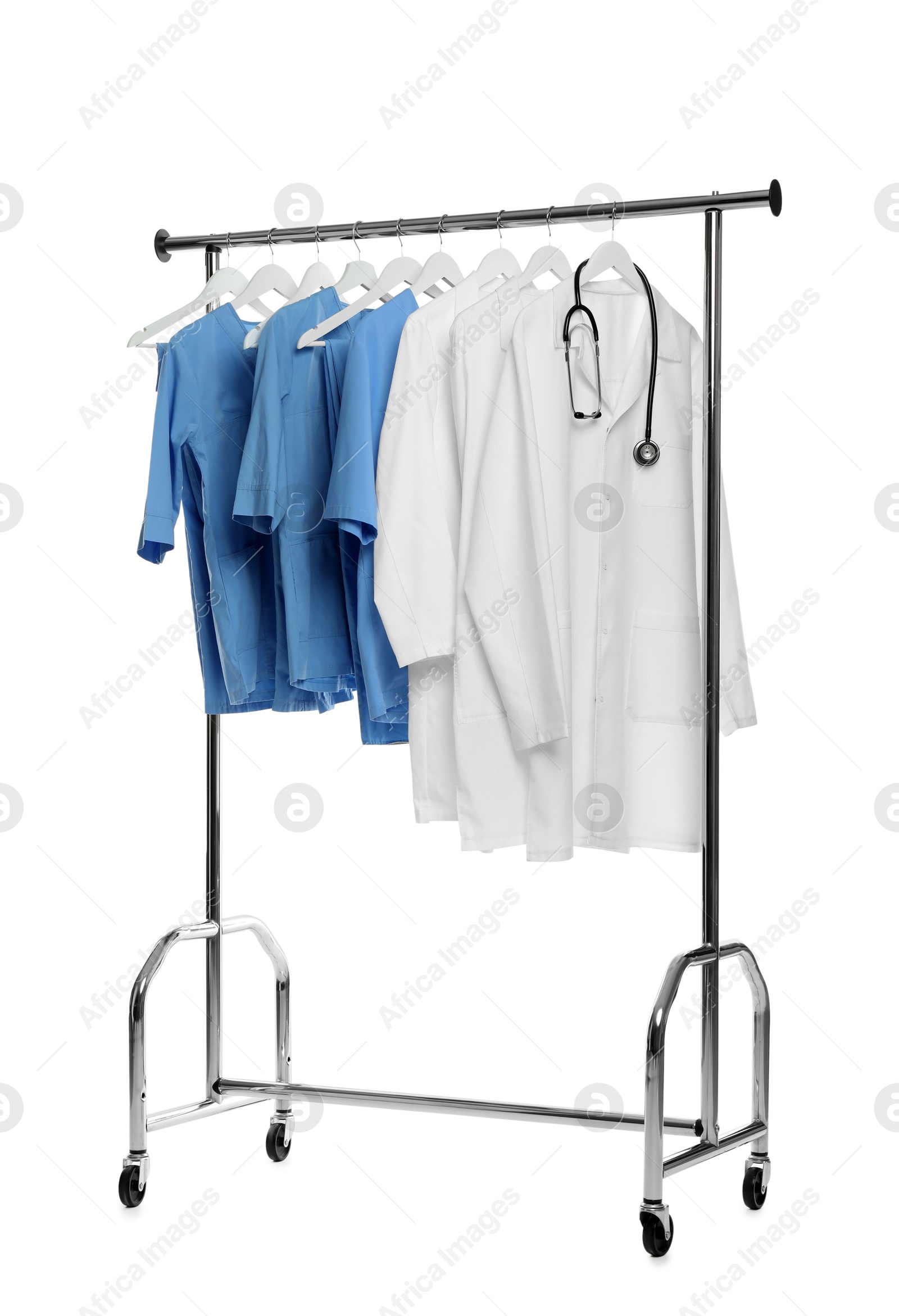 Photo of Different medical workers' uniforms and stethoscope on clothing rack against white background