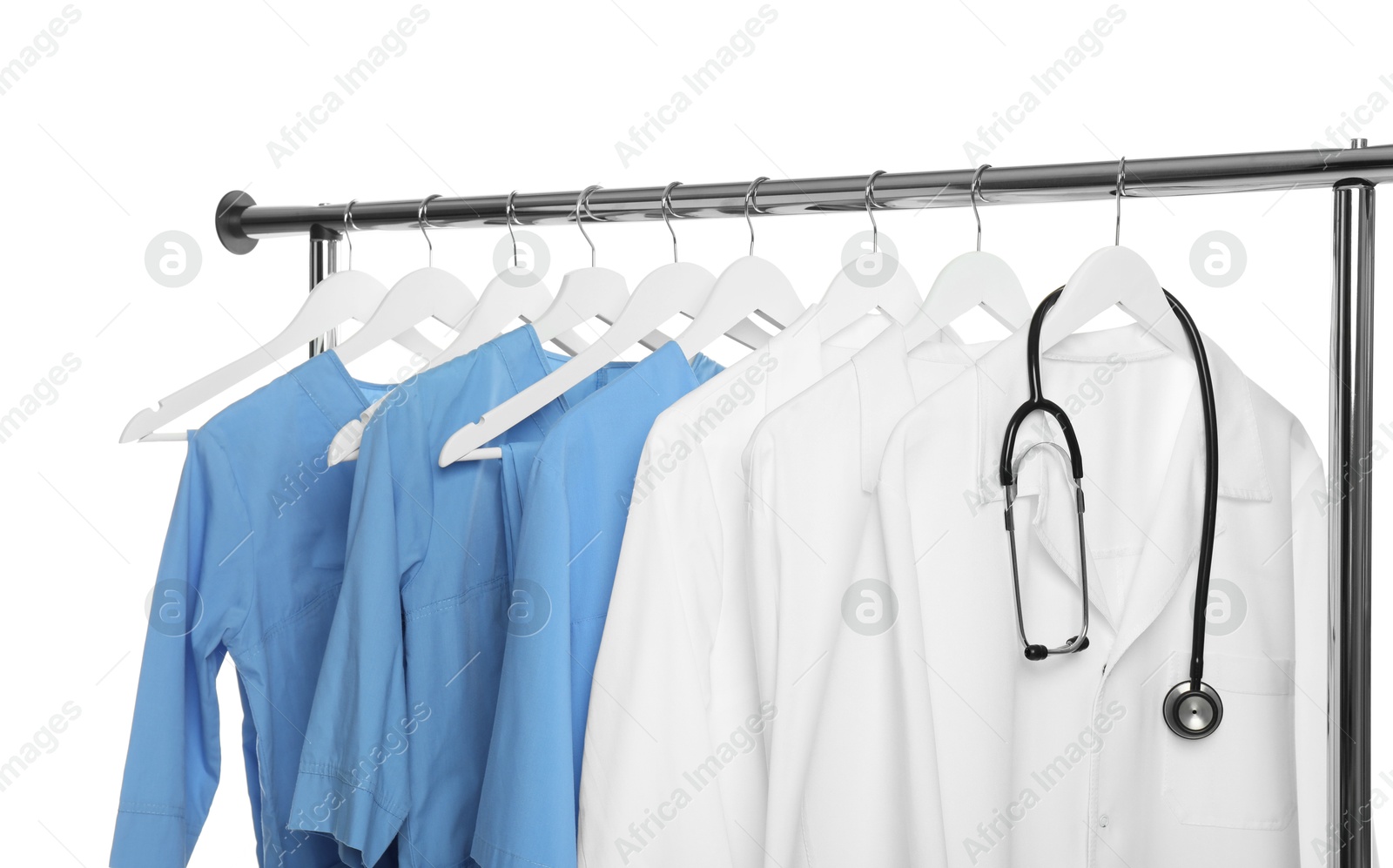 Photo of Different medical workers' uniforms and stethoscope on clothing rack against white background