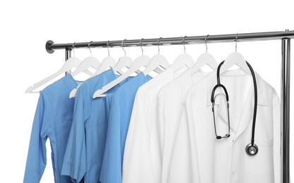 Photo of Different medical workers' uniforms and stethoscope on clothing rack against white background