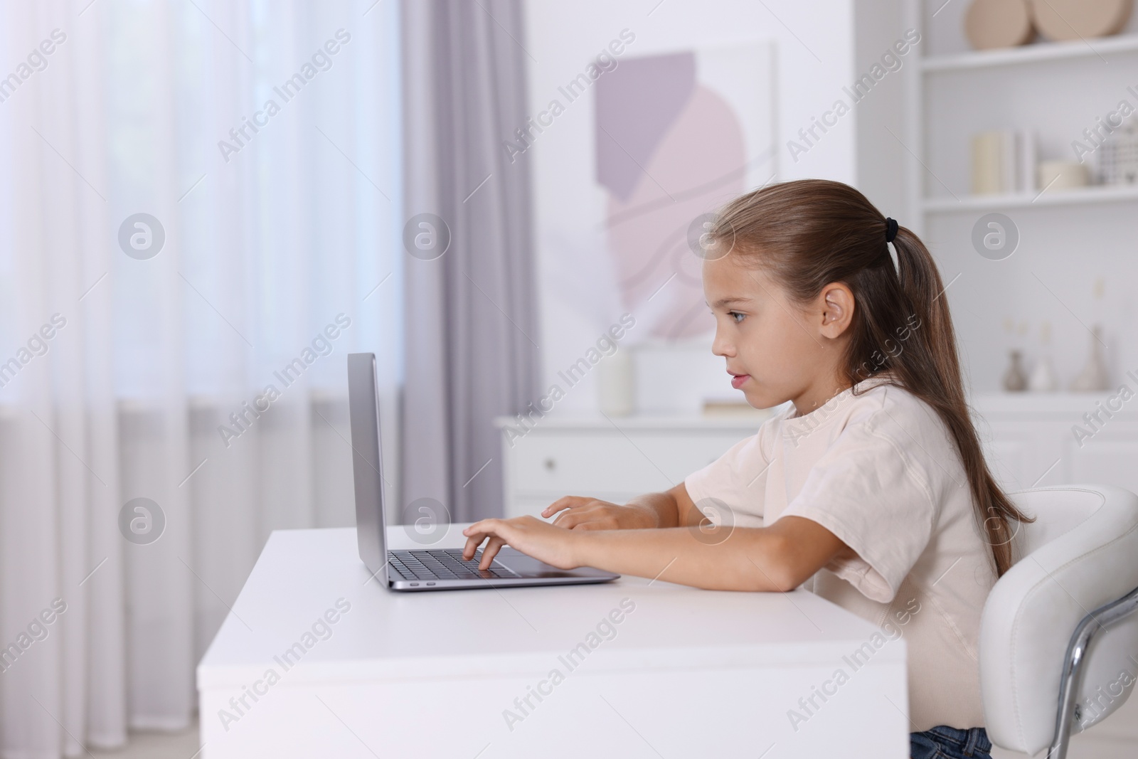 Photo of Girl with incorrect posture using laptop at white desk indoors