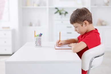 Photo of Boy with correct posture doing homework at white desk indoors