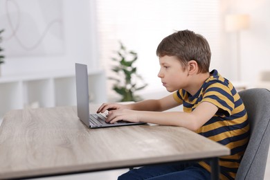 Boy with incorrect posture using laptop at wooden desk indoors